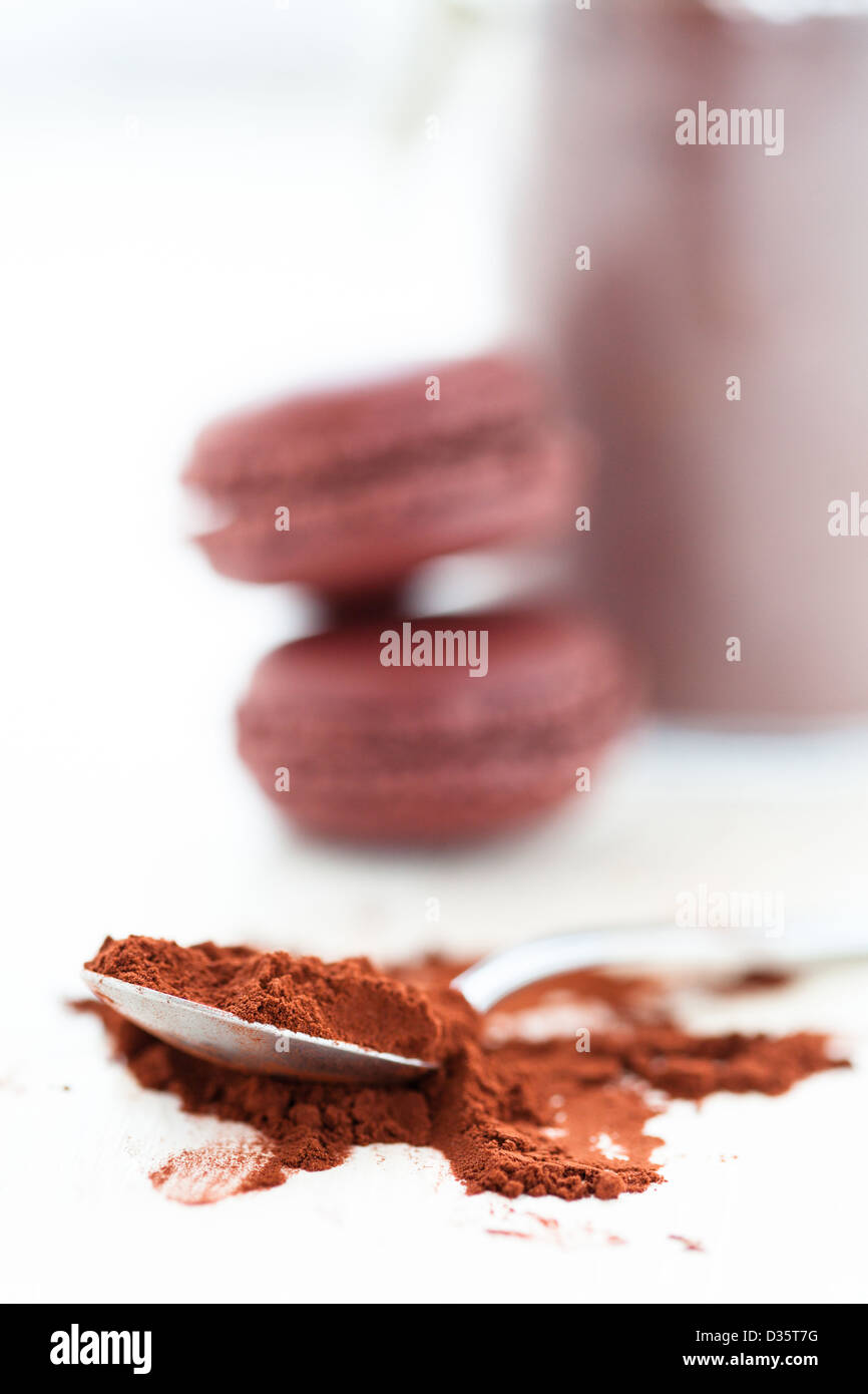 Nahaufnahme von Kakaopulver und Löffel mit zwei Makronen und Glas im Hintergrund Stockfoto