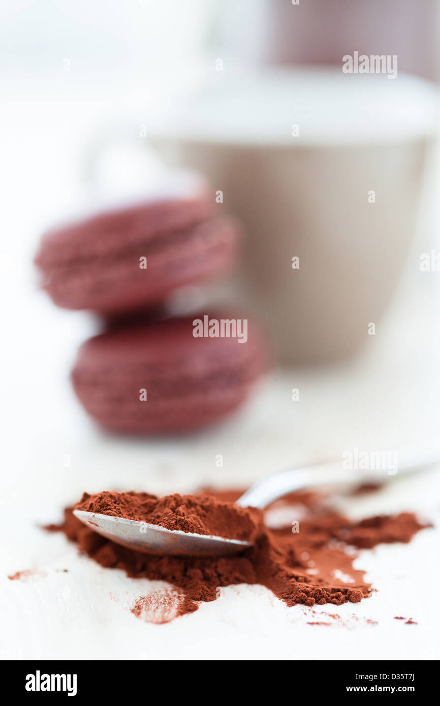 Nahaufnahme von Kakaopulver und Löffel mit zwei Makronen und Becher und Glas Jar im Hintergrund Stockfoto