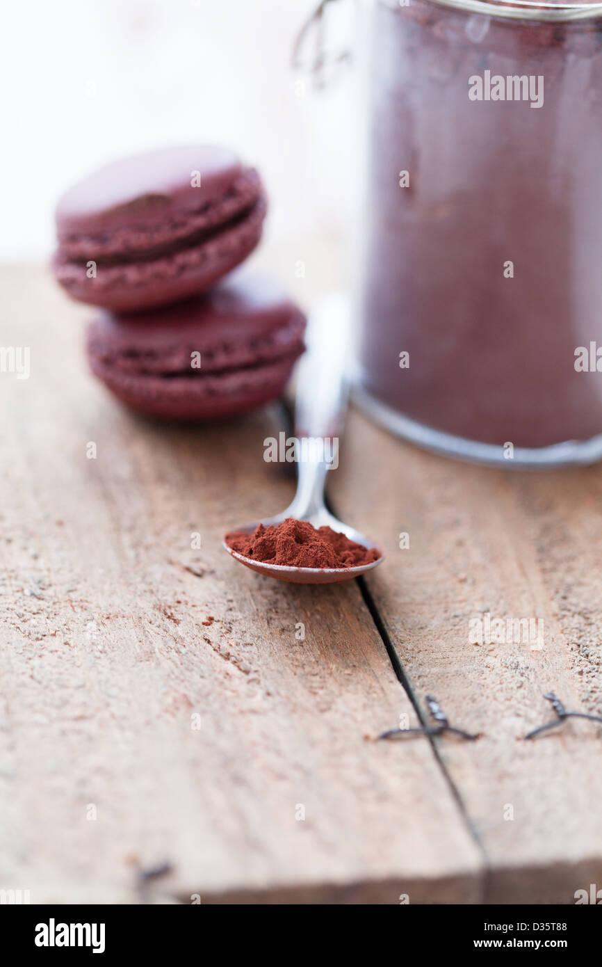 Nahaufnahme von Kakaopulver in Löffel mit zwei Makronen und Glas im Hintergrund Stockfoto