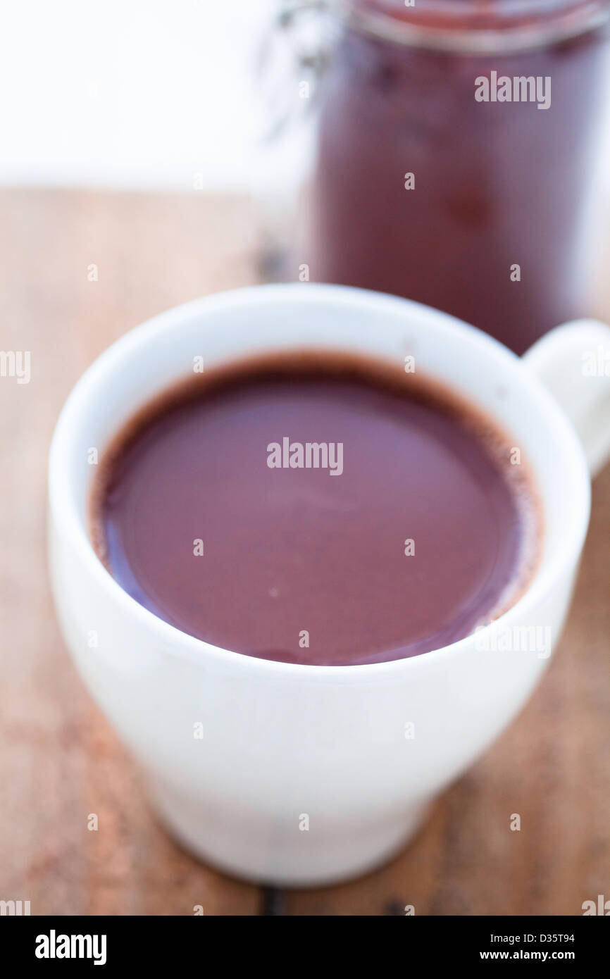 Nahaufnahme der Tasse heißer Schokolade auf einem Holztisch mit Kakaopulver in Glas im Hintergrund Stockfoto