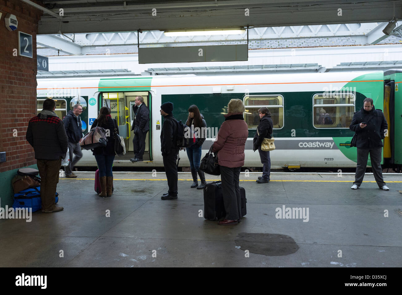 Eine Bahn Wache auf dem Handy eine Verzögerung, die Zugverbindung zu diskutieren, während Passagiere auf der platform.14/01/2013 in Worthing Station warten. Bild von Julie Edwards Stockfoto