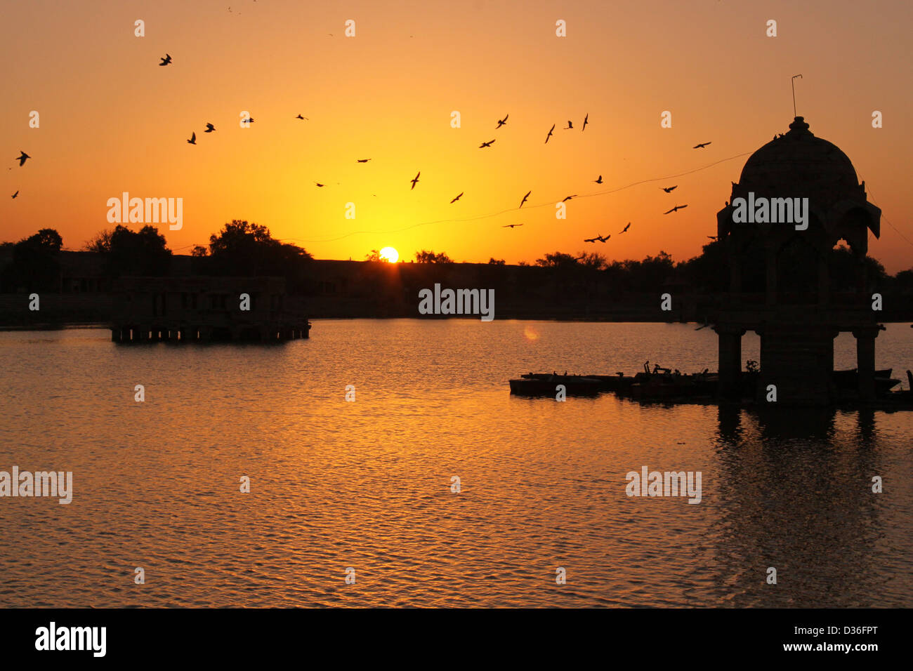 Sonnenaufgang am Gadi Sagar See mit Silhouette der Kuppel in der Mitte und die Vögel fliegen, Rajasthan Indien Stockfoto