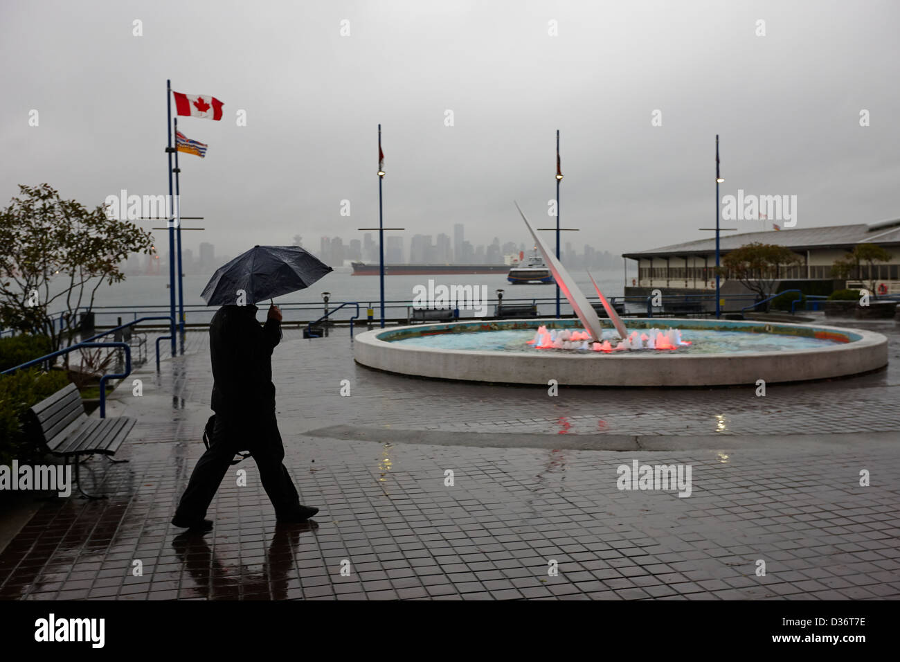 Mann mit Schirm zu Fuß in Richtung Seabus terminal in den Regen North Vancouver BC Kanada Stockfoto