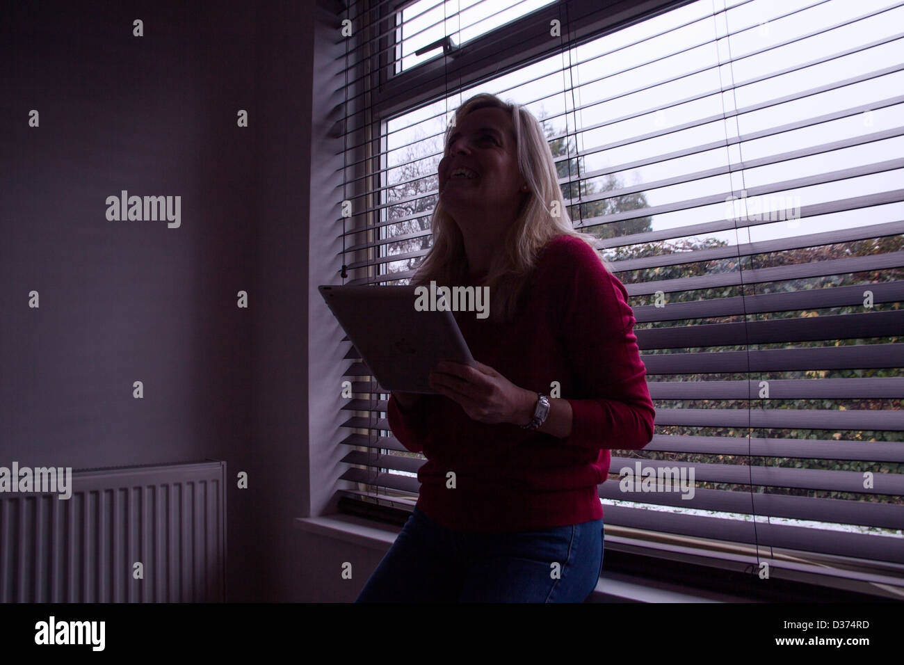 Sihouette eine blonde Frau mit einem digital-Tablette, ist das Licht in streaming, hinter ihr wie sie schaut und lacht. Stockfoto