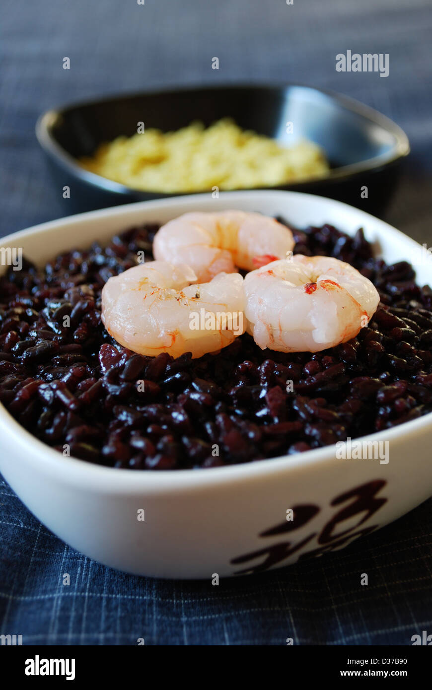 Schwarzer Reis mit Garnelen und Kichererbsen-Creme in weißen Schalen auf grauem Hintergrund Stockfoto