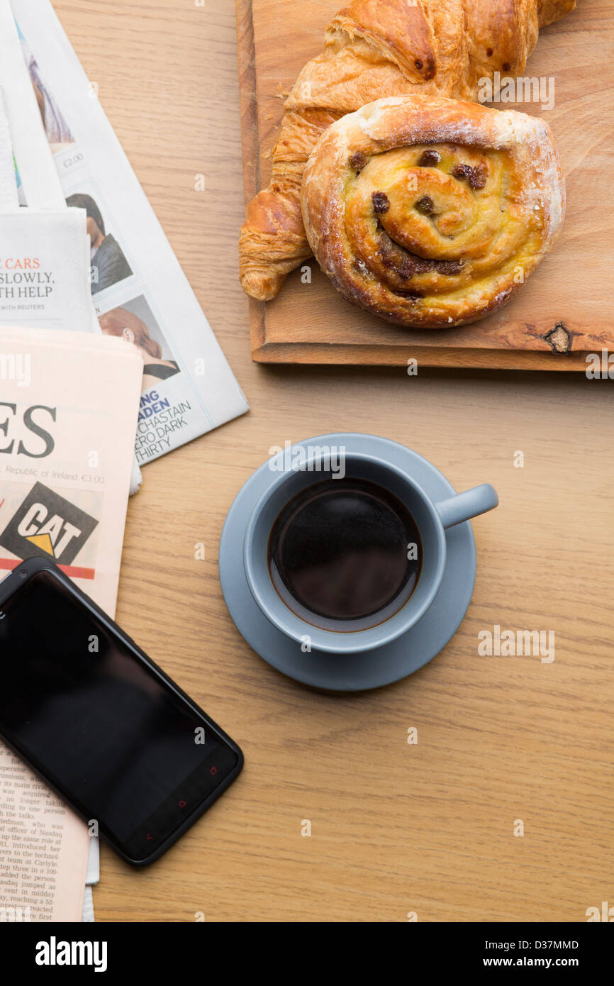 Frisches Gebäck Espresso und ein HTC One X + Handy mit einer Kopie der Financial Times Zeitung auf eine Holzoberfläche. Stockfoto