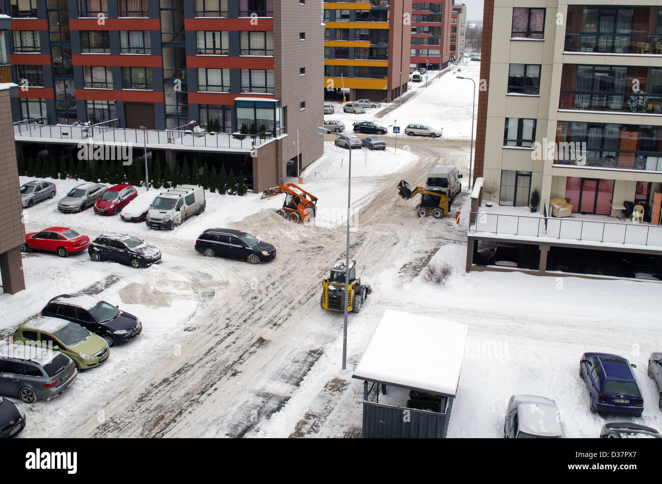 kleiner Traktor Bagger Bobcat Arbeit sauber Schnee zwischen flachen Blockhäuser auf Straße pa Stockfoto
