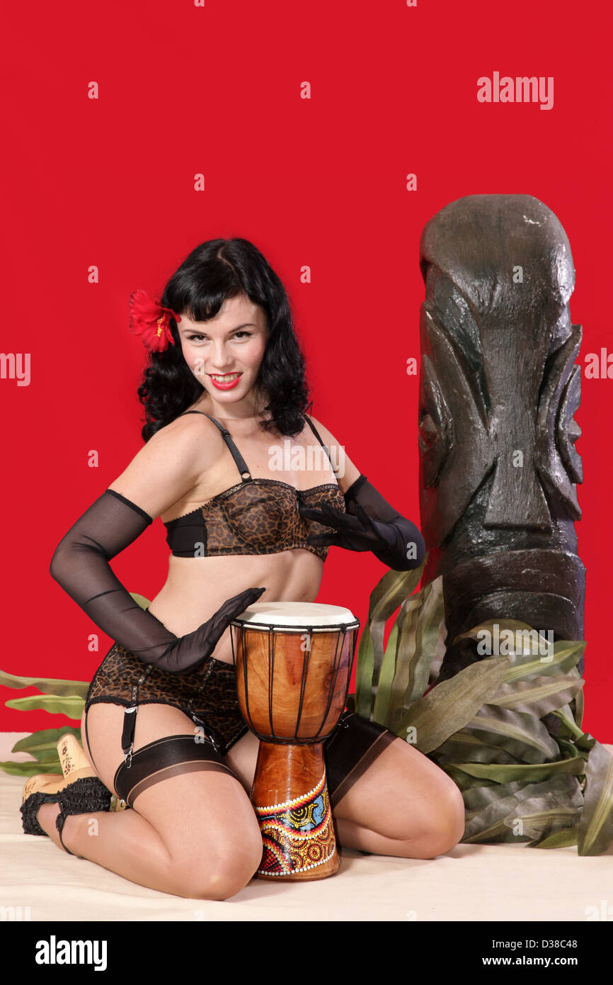 Sexy Pinup-Girl spielt Bongo Trommel neben einer Tiki statue Stockfoto