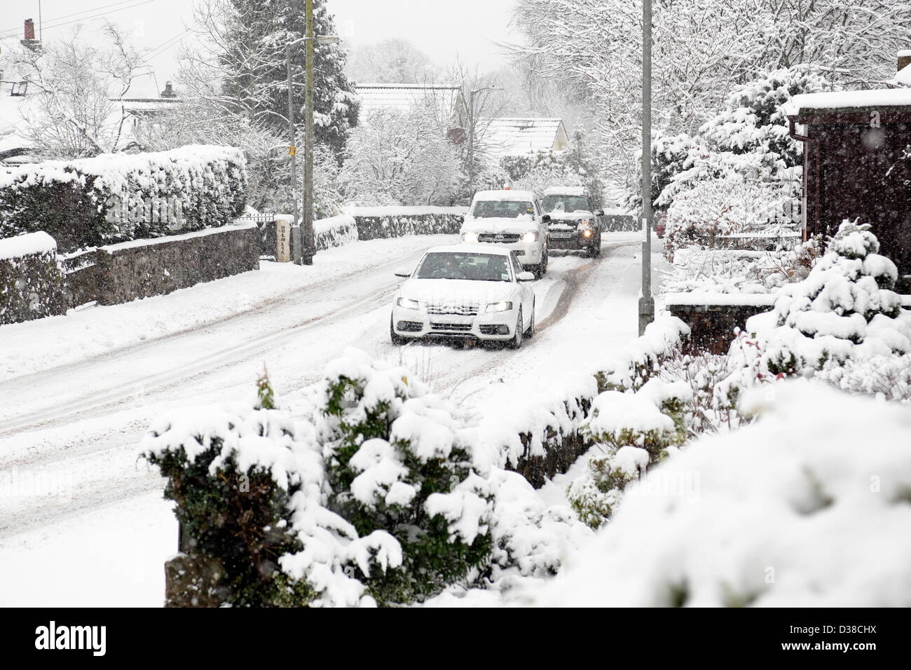 Johnshill, Lochwinnoch, Renfrewshire, Schottland, Großbritannien, Mittwoch, 13th. Februar 2013. Autos fahren im fallenden Schnee auf der Hauptstraße durch das Dorf. Stockfoto