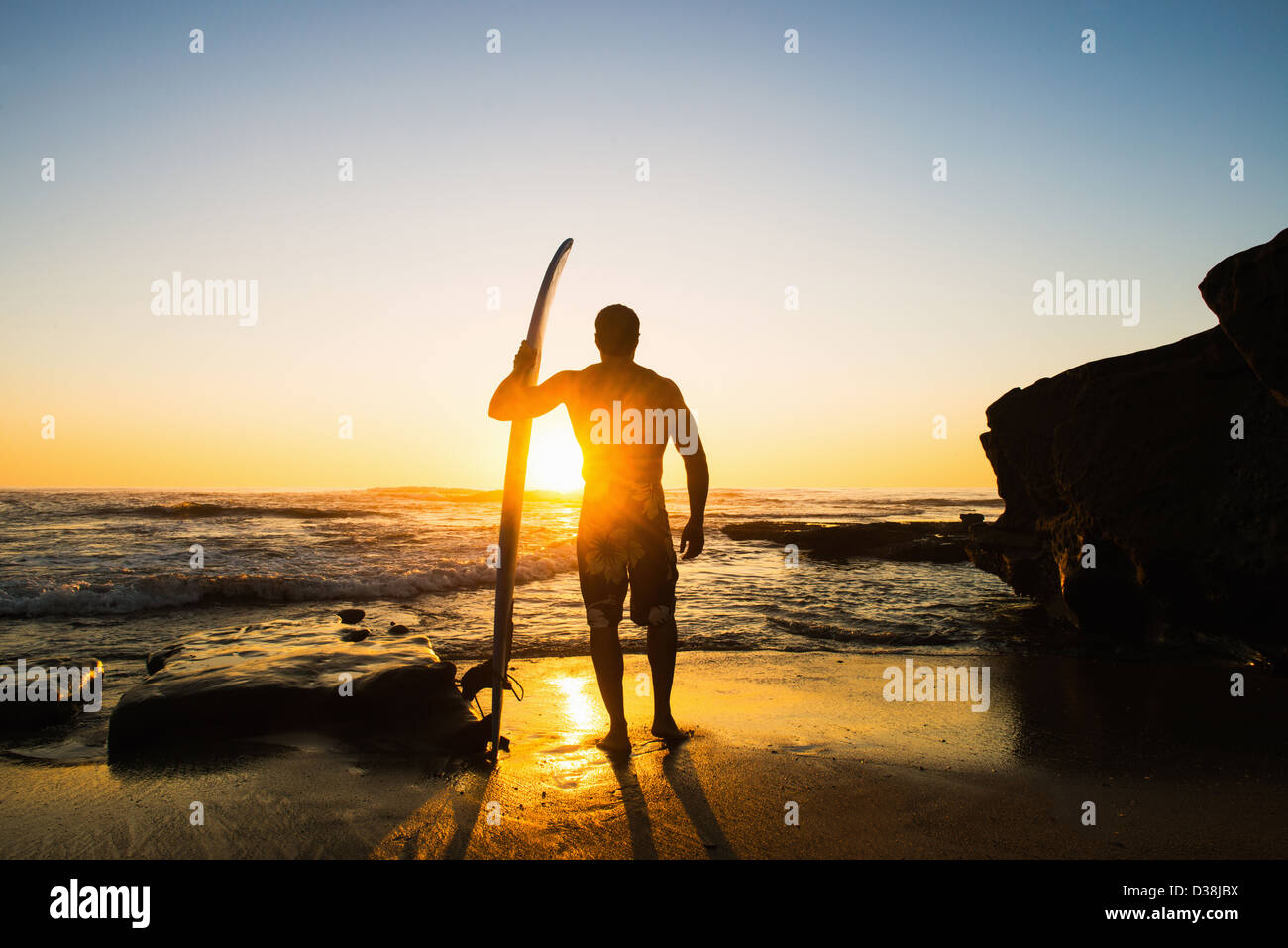 Mann mit Surfbrett auf felsigen Strand Stockfoto