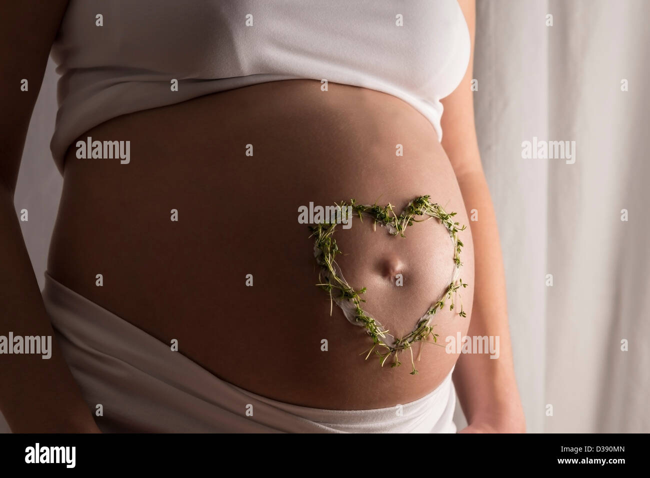 Junge Frau mit weißen Kleidern und eine Creme und Kresse Herzen auf ihrem Baby-Bauch Stockfoto