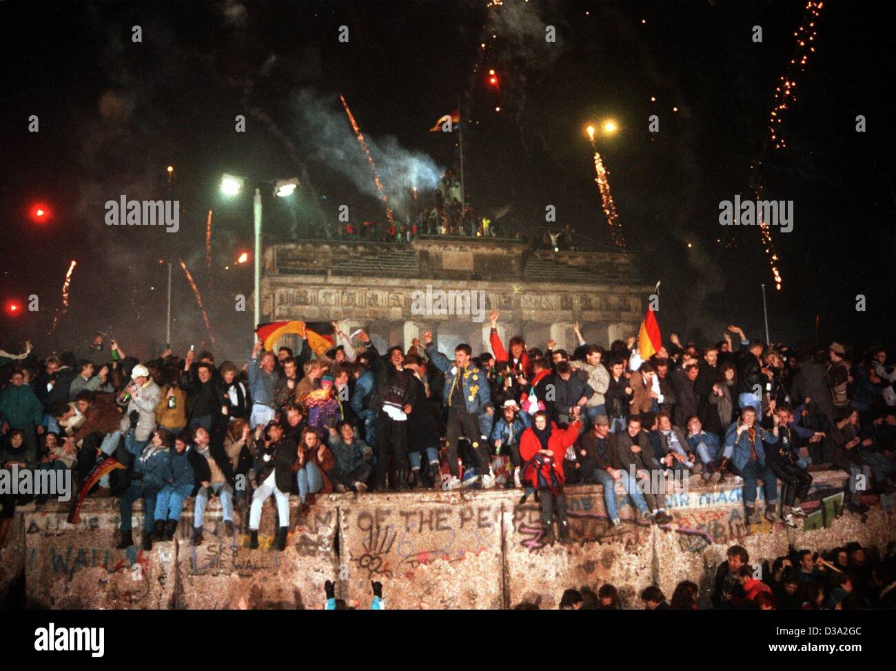 (Dpa-Dateien) - Menschen sitzen und stehen auf der Berliner Mauer vor dem "Brandenburger Tor", feiert das neue Jahr und die Öffnung der Mauer im November, 1. Januar 1990. Stockfoto