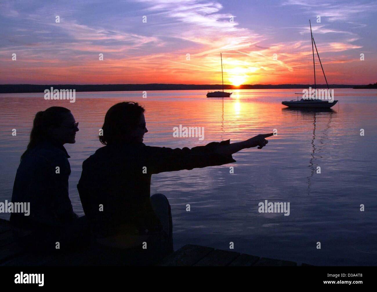 (Dpa) - zwei junge Frauen sehen den malerischen Sonnenuntergang vom Ufer des Ammersee in Bayern, Deutschland, 13. Juni 2002. Stockfoto