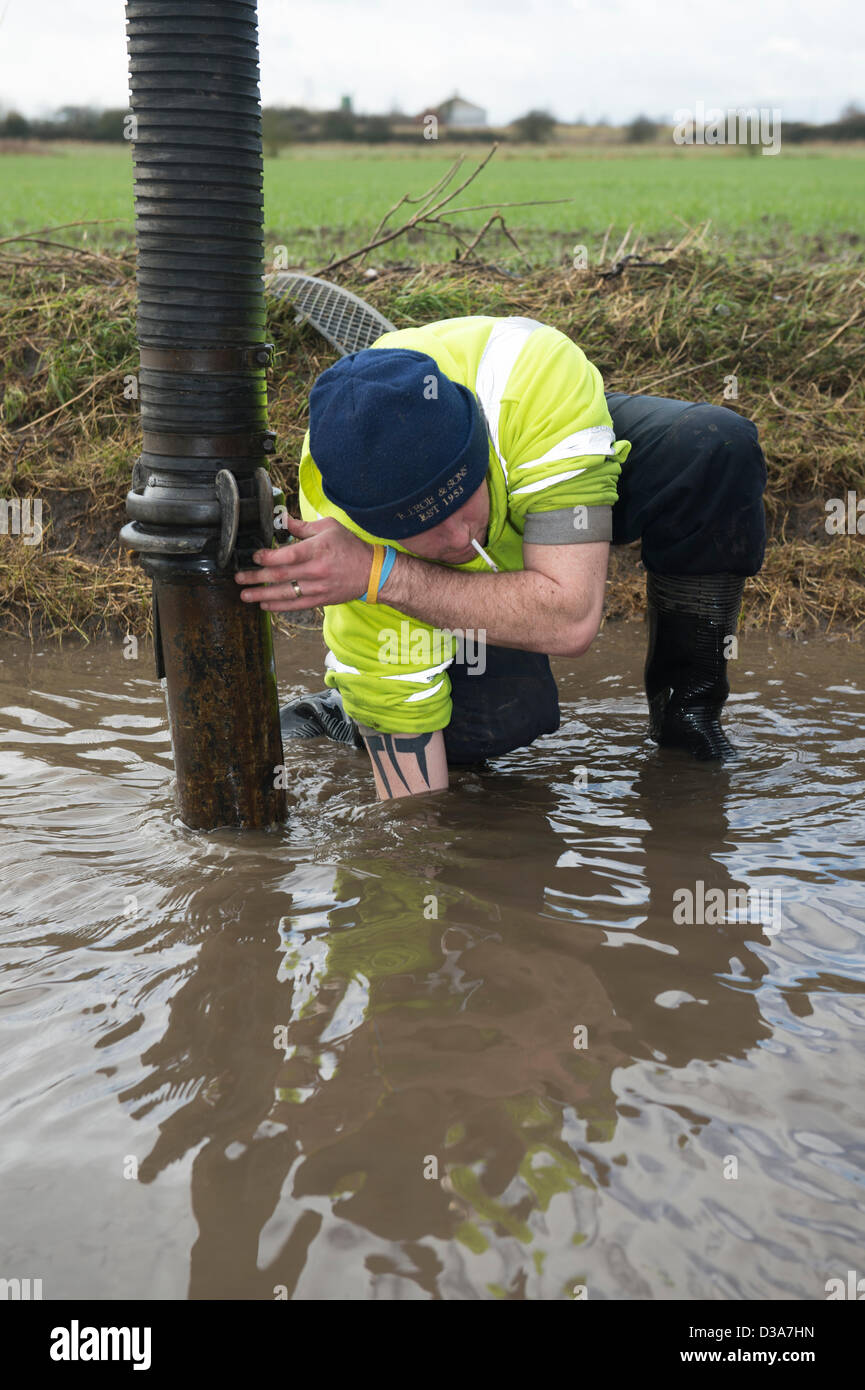 Ein Arbeiter Aufräumen der verstopften Abflüssen in einen Feldweg als ein Build von Schlick hat langfristige Überschwemmungen und Road Verschlüsse verursacht. Stockfoto