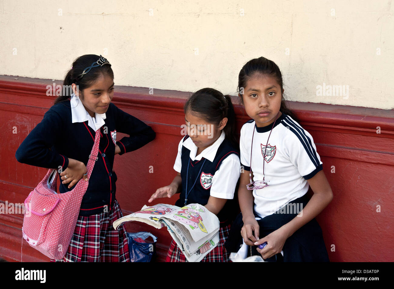 3 junge mexikanische Schulmädchen auf Straße in Schuluniformen mit karierten Röcken gekleidet betrachten ein Malbuch Oaxaca Mexico Stockfoto