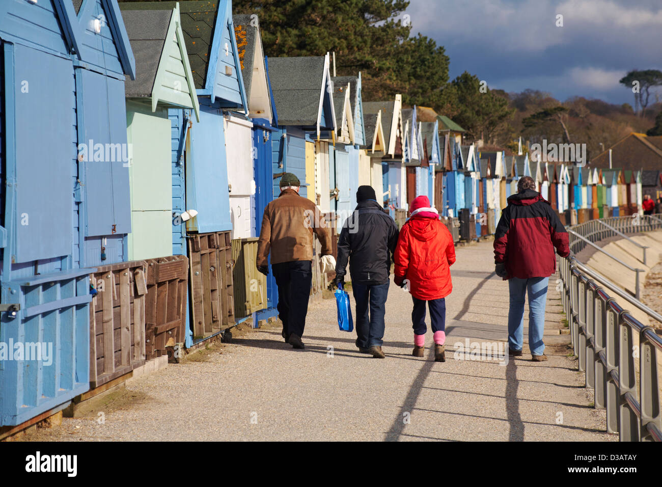 Menschen, die an Strandhütten in Avon Beach, Mudeford, Christchurch, Dorset UK im Februar entlang der Promenade spazieren Stockfoto