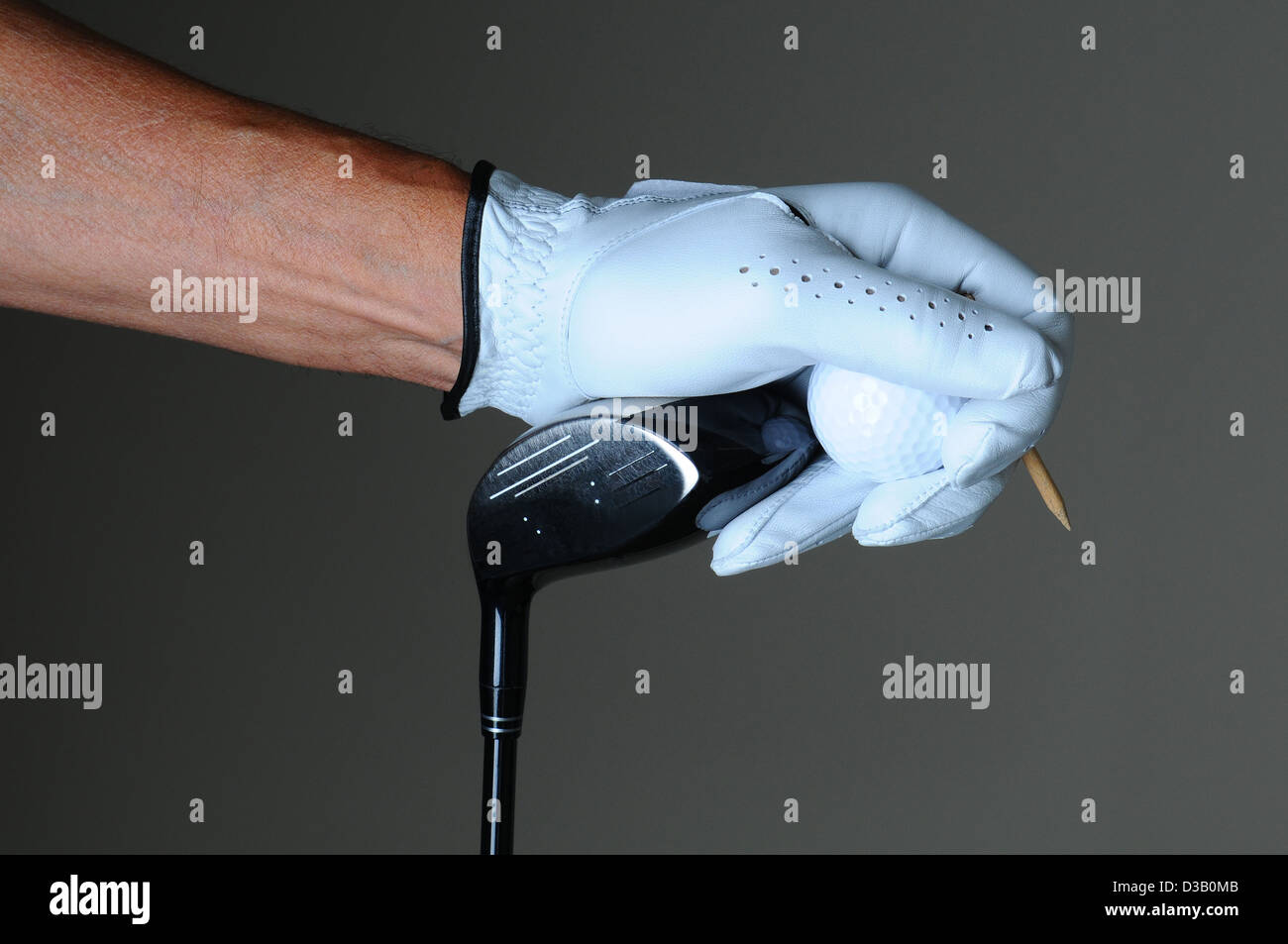 Nahaufnahme einer Golfer Hand hält einen Schlägerkopf, Golfball und Abschlag über eine leichte ot dunkelgrauen Hintergrund. Stockfoto