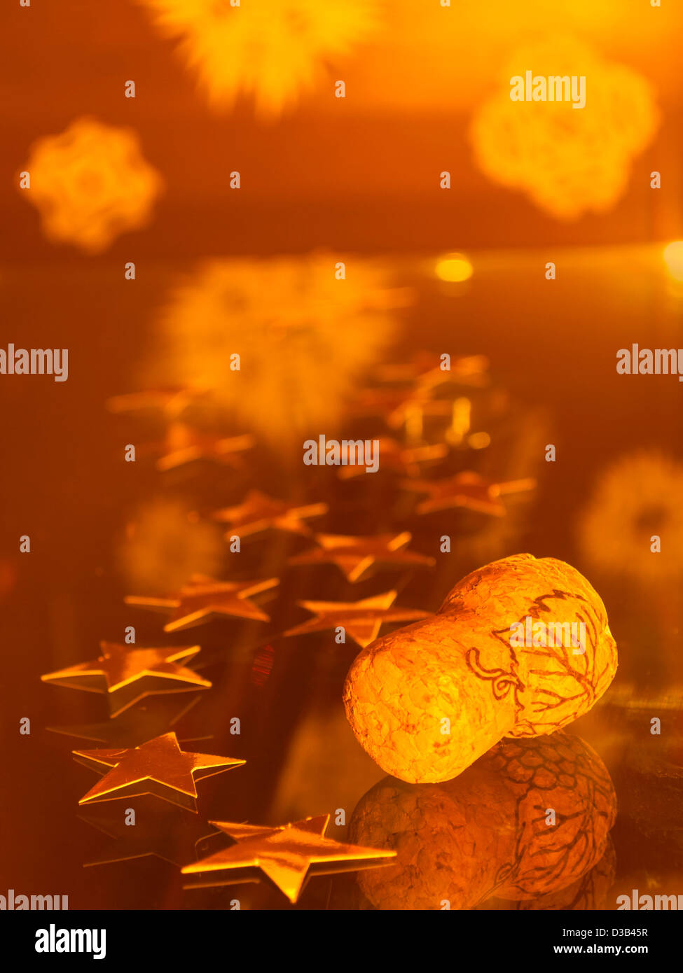 Sektkorken und goldene Sterne legen auf Glasoberfläche mit Papier Schneeflocken hinter; Kork im Fokus Stockfoto