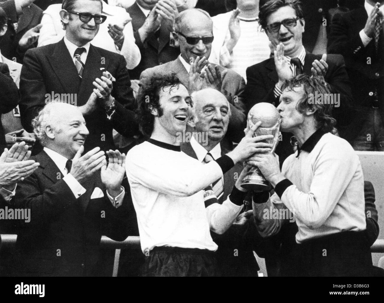 (Dpa-Dateien) - Franz Beckenbauer (2. v. L), dann deutsche Mannschaftskapitän und Torhüter Sepp Maier (R) ihre Trophäe, schätzen während deutsche Präsident Walter Scheel (L) begrüßt, nachdem Deutschland die Fußball-Weltmeisterschaft in München, 7. Juli 1974 gewann. Deutschland besiegt die Niederlande im Finale mit 2:1. Stockfoto