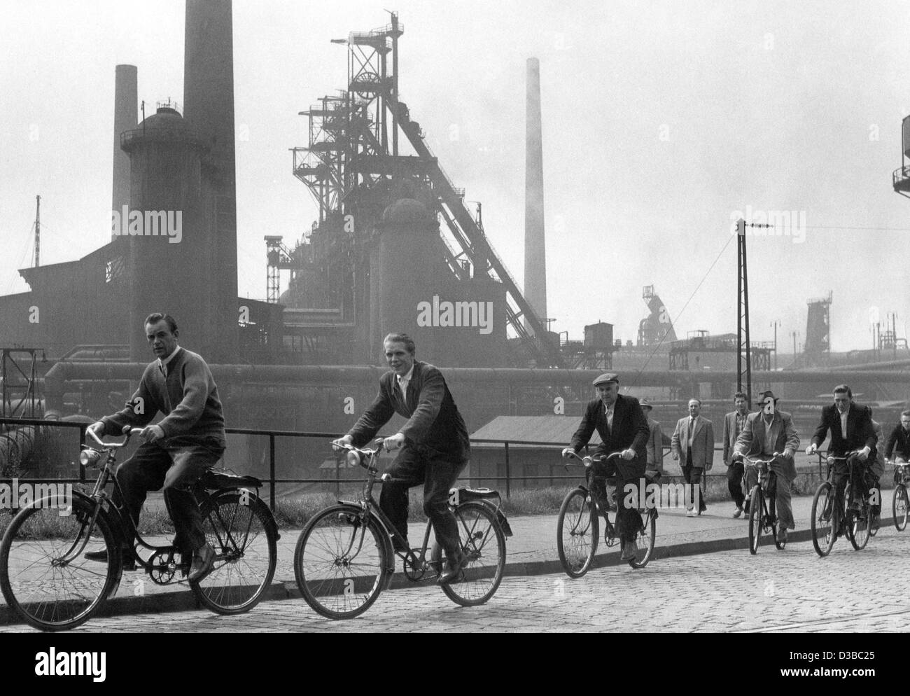 (Dpa-Dateien) - Nachdem die Schichtarbeiter Umstellung auf ihren Bikes die Hüttenwerken in Oberhausen, Deutschland, 1957 passieren. Stockfoto