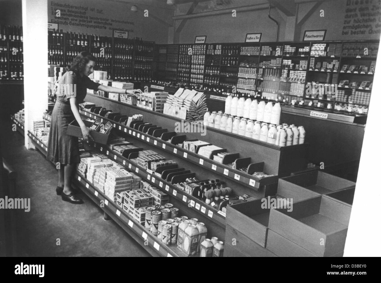 (Dpa-Dateien) - ein Kunde mit einer Holzkiste Geschäfte im ersten selbst service-Shop, der sich in Augsburg, Deutschland, 7. Juni 1949 eröffnet wurde. Auf der rechten Seite einen Haufen von leeren Holzkisten sind für Shopper gestapelt. Der Shop "Bern. Müller ", wo Kunden ihre eigenen Produkte ausgewählt und bezahlt die Stockfoto