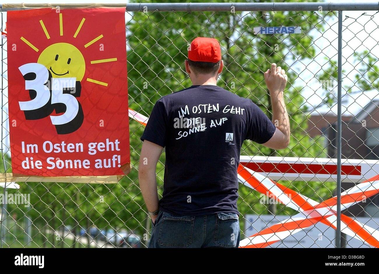 (Dpa) - Stürmer steht an einem Zaun neben ein Plakat im Osten Geht Die Sonne Auf liest "(die Sonne geht im Osten) in den Räumlichkeiten des VW-Werk in Mosel, Deutschland, 4. Juni 2003. Die Nummer 35 auf dem Plakat symbolisiert den Grund für den Arbeitskampf, die über die Introducti ist Stockfoto