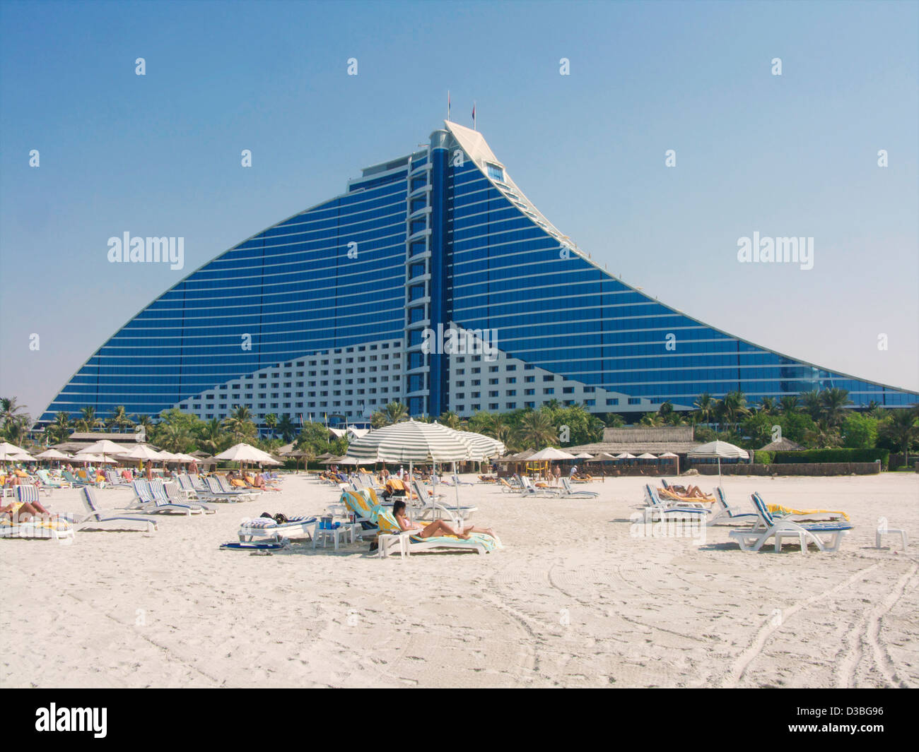 Der Strand vor dem Jumeirah Beach Hotel in Dubai UAE mit Liegestühlen und Sonnenschirmen mit Sonne Badegäste auf sie. Stockfoto