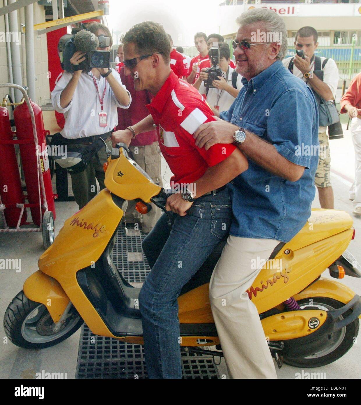 (Dpa) - kommt deutsche Formel-1-Weltmeister Michael Schumacher (vorne) mit seinem Manager Willi Weber auf einem Motorroller in Interlagos Formel 1 Rennstrecke in Sao Paulo, Brasilien, 3. April 2003. Der brasilianischen Formel Eins grand Prix ist das dritte Formel 1 Rennen nach Australien und Malaysia gr Stockfoto