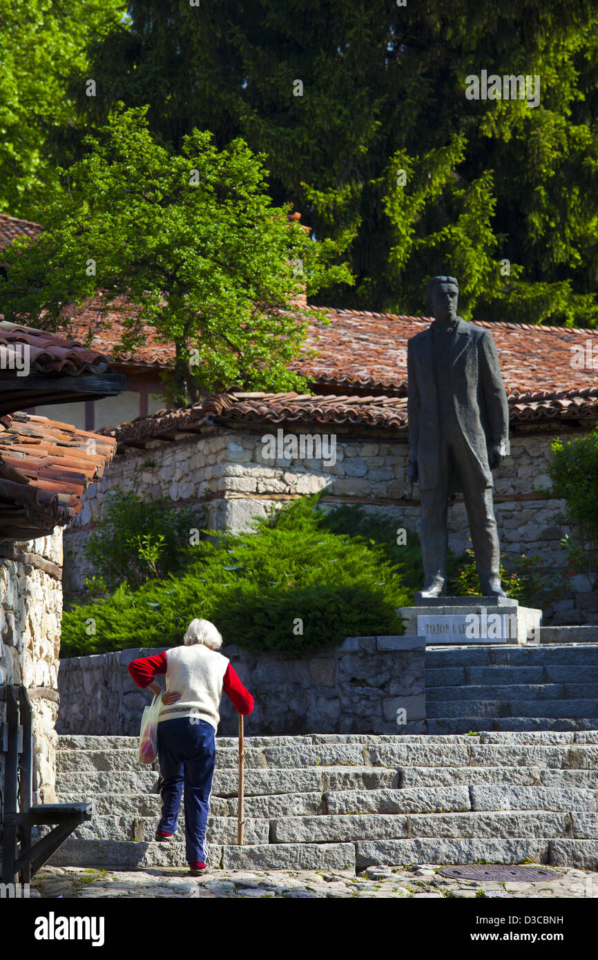 Bulgarien, Europa, Koprivshtitsa, Dimcho Debelianov Straße, alte Frau, die zu Fuß in Richtung Statue von Todor Kableshkov. Stockfoto