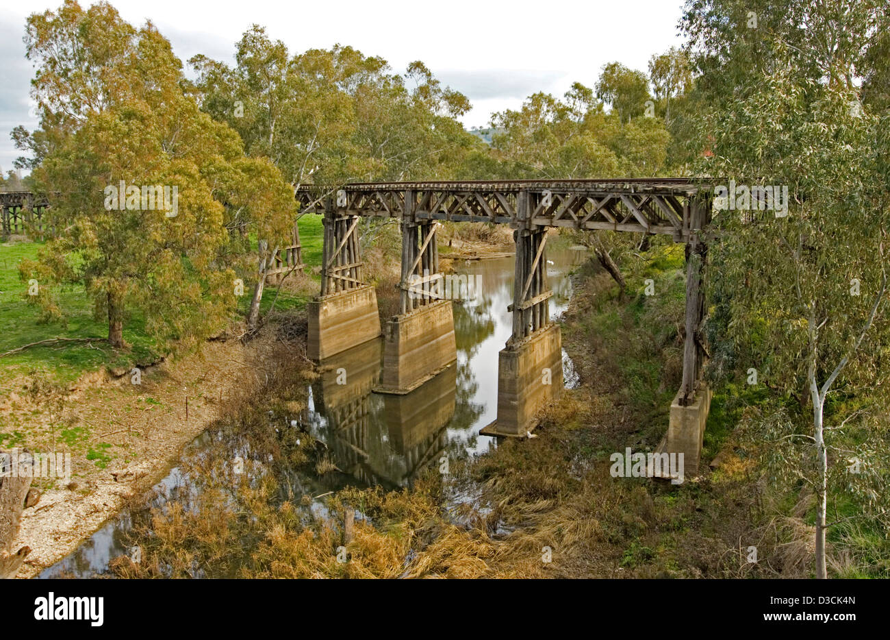 Historischen hölzernen Bock Eisenbahnbrücke durch Wald und reflektierte im ruhigen Wasser des schmalen Bach weit unten am Gundagai, NSW Stockfoto