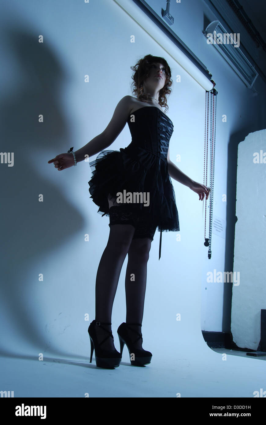 Hohe Modell Silhouette einer Frau in einer Studioumgebung mit Hintergrund in kurzen schwarzen Kleid posiert mit high Heels für Mode erschossen Stockfoto