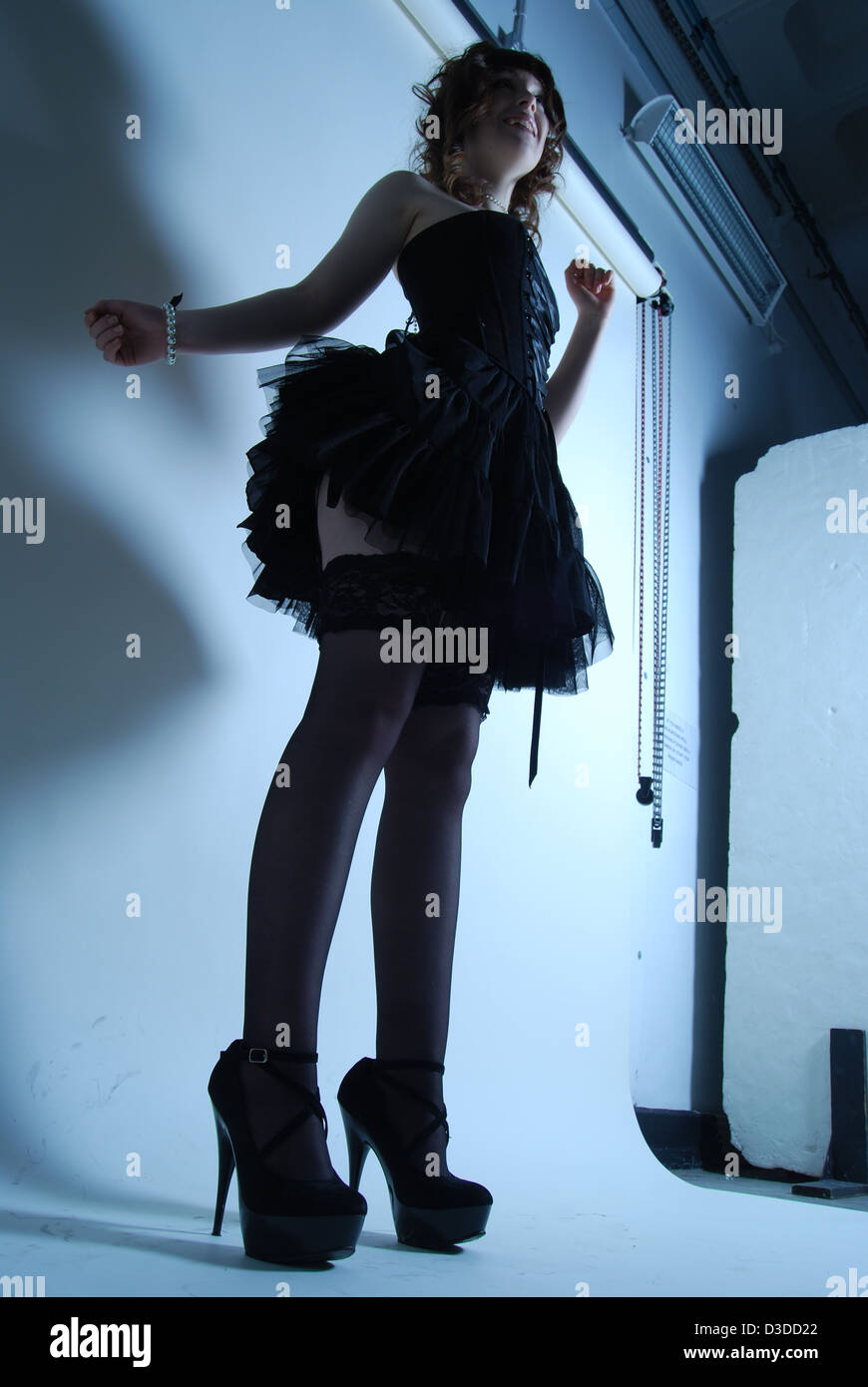 Hohe Modell Silhouette einer Frau in einer Studioumgebung mit Hintergrund in kurzen schwarzen Kleid posiert mit high Heels für Mode Stockfoto