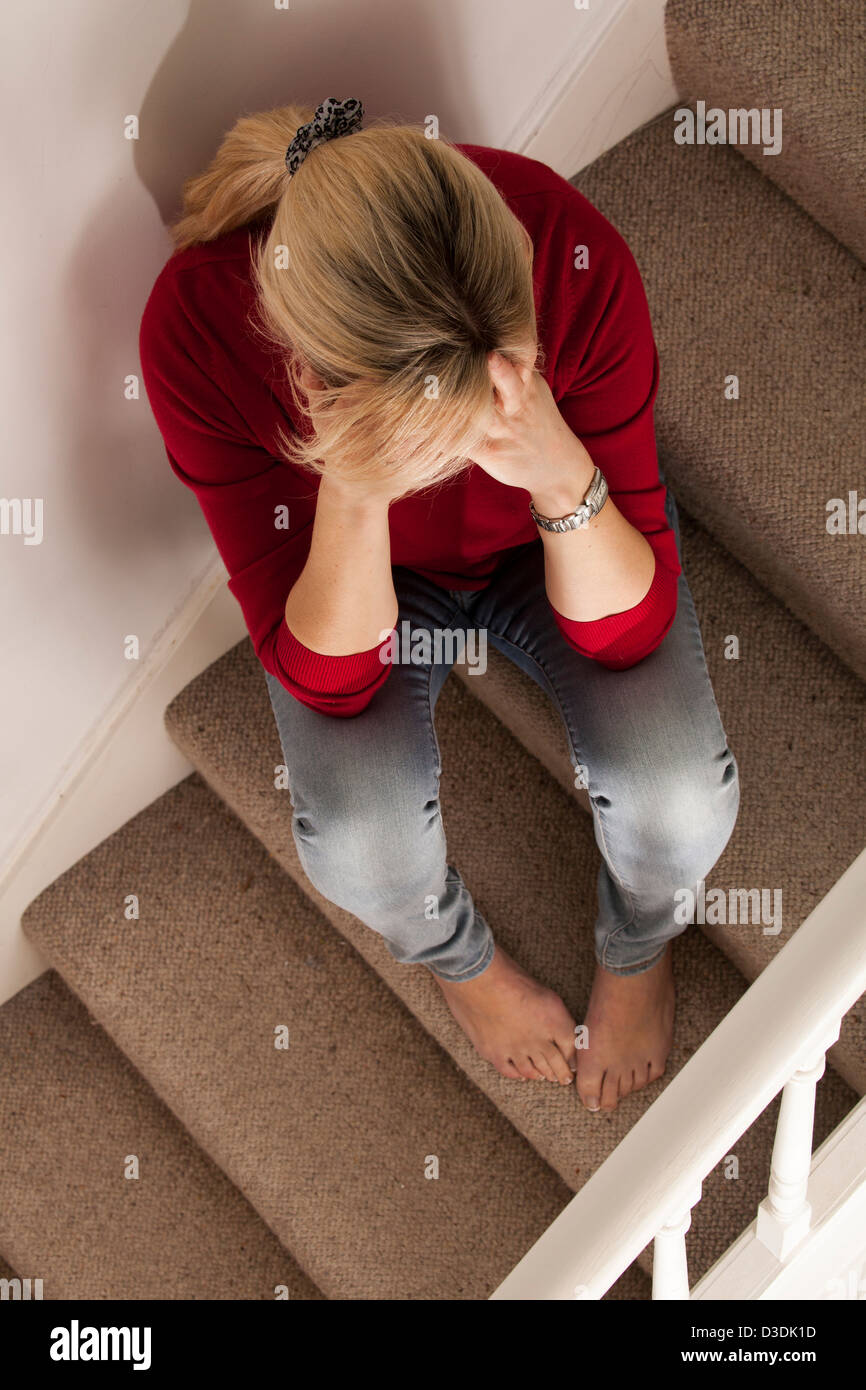 Frau mit blonden Haaren, Kopf in ihre Hände. Sitzt auf der Treppe, von oben gesehen. Stockfoto