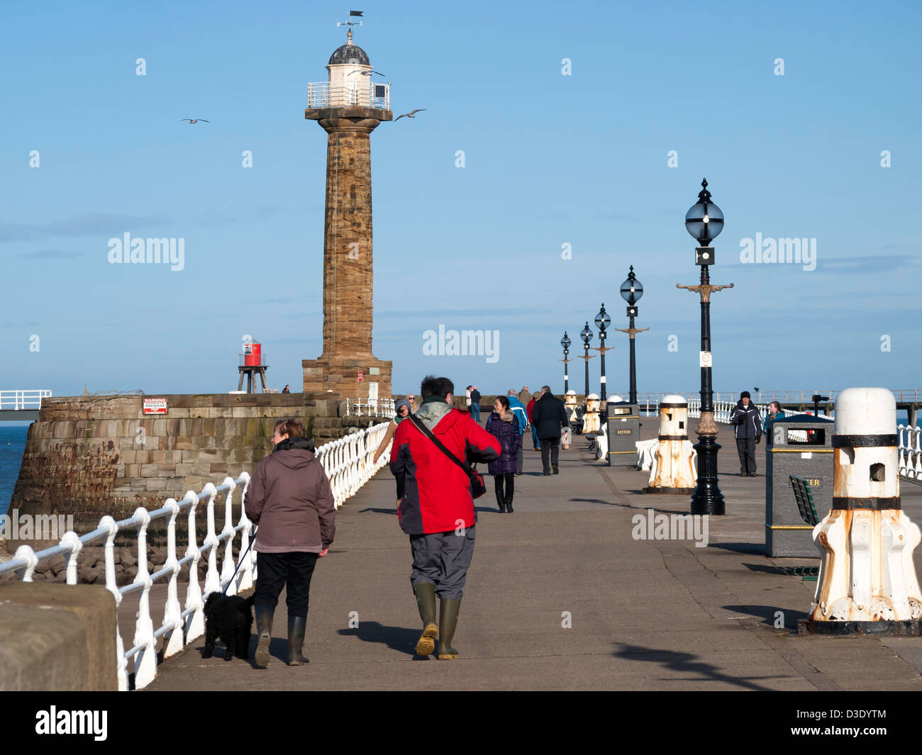 Touristen auf Whitby West Pier und Leuchtturm an einem sonnigen Wintertag Stockfoto