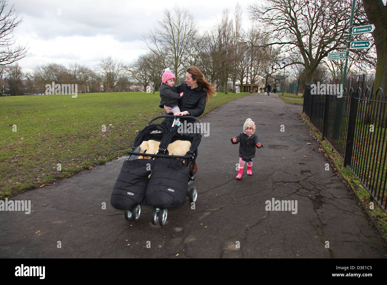 Junge Mutter im Park schieben einen Twin Buggy mit ihren zwei Kleinkinder. Stockfoto