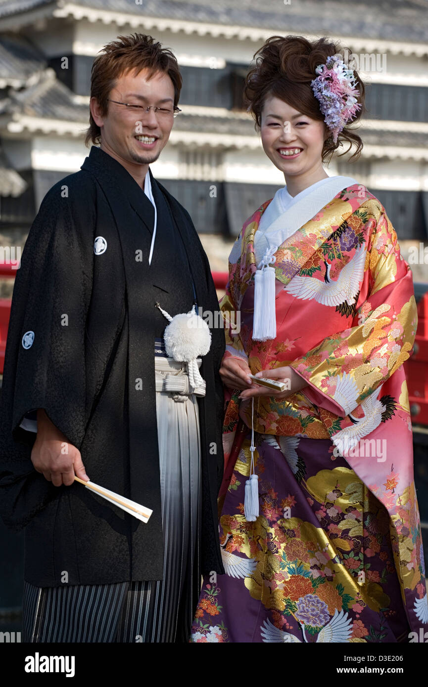 Eine glückliche japanische Braut und Bräutigam im traditionellen Hochzeitskimono, während sie vor dem Schloss Matsumoto in Nagano posieren. Stockfoto
