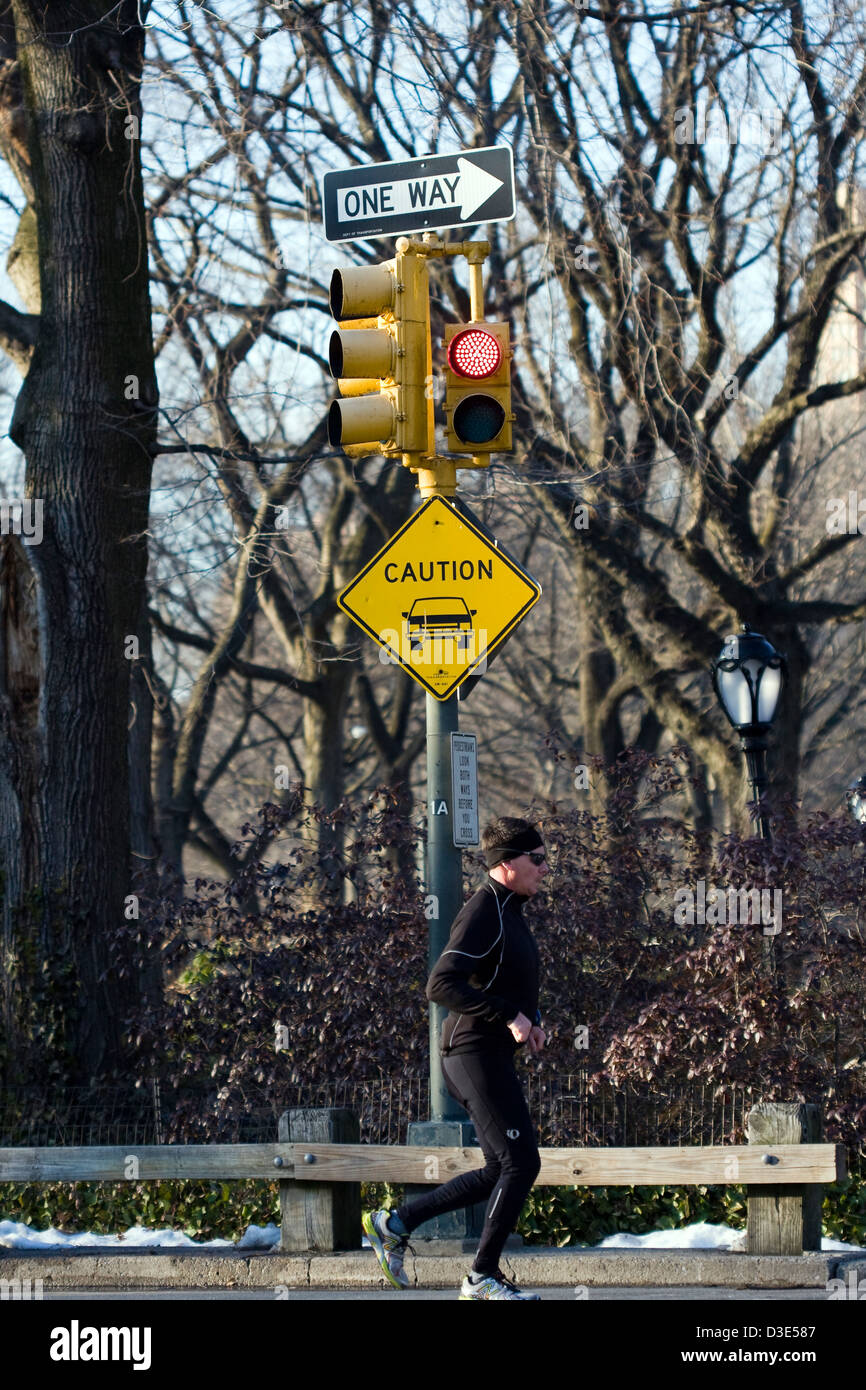 Läufer Joggen vorbei an "One Way" und "Vorsicht Motor Vehicle" Zeichen auf eine Ampel im New Yorker Central Park Stockfoto