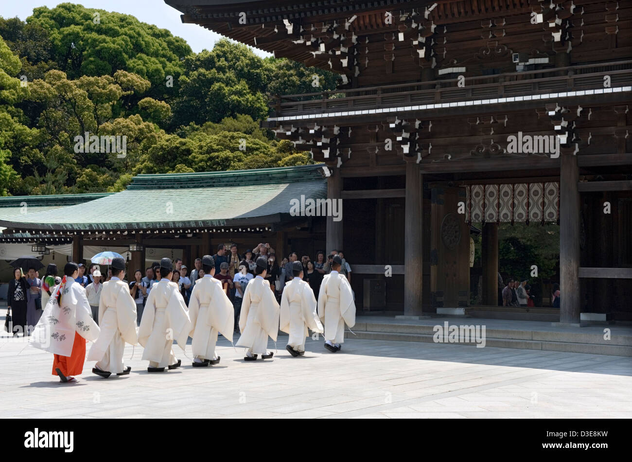 Shinto-Priester und ein Miko-Mädchen im roten Gewand in Prozession durch Haupttor des Meiji-Jingu Schrein während einer religiösen Zeremonie Stockfoto