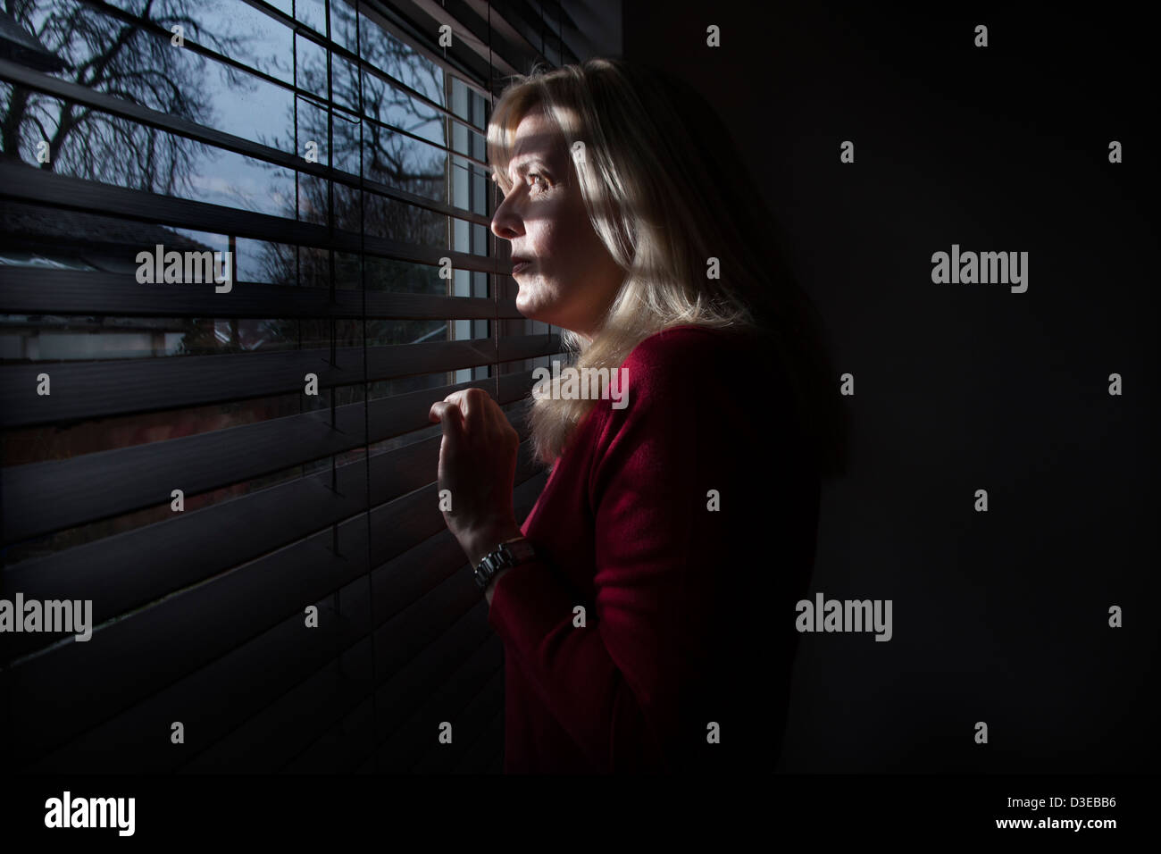 Profil einer Frau im Schatten Blick durch ein Fenster Licht strömt durch die Blinds auf ihr Gesicht. Modelleigenschaft veröffentlicht. Stockfoto