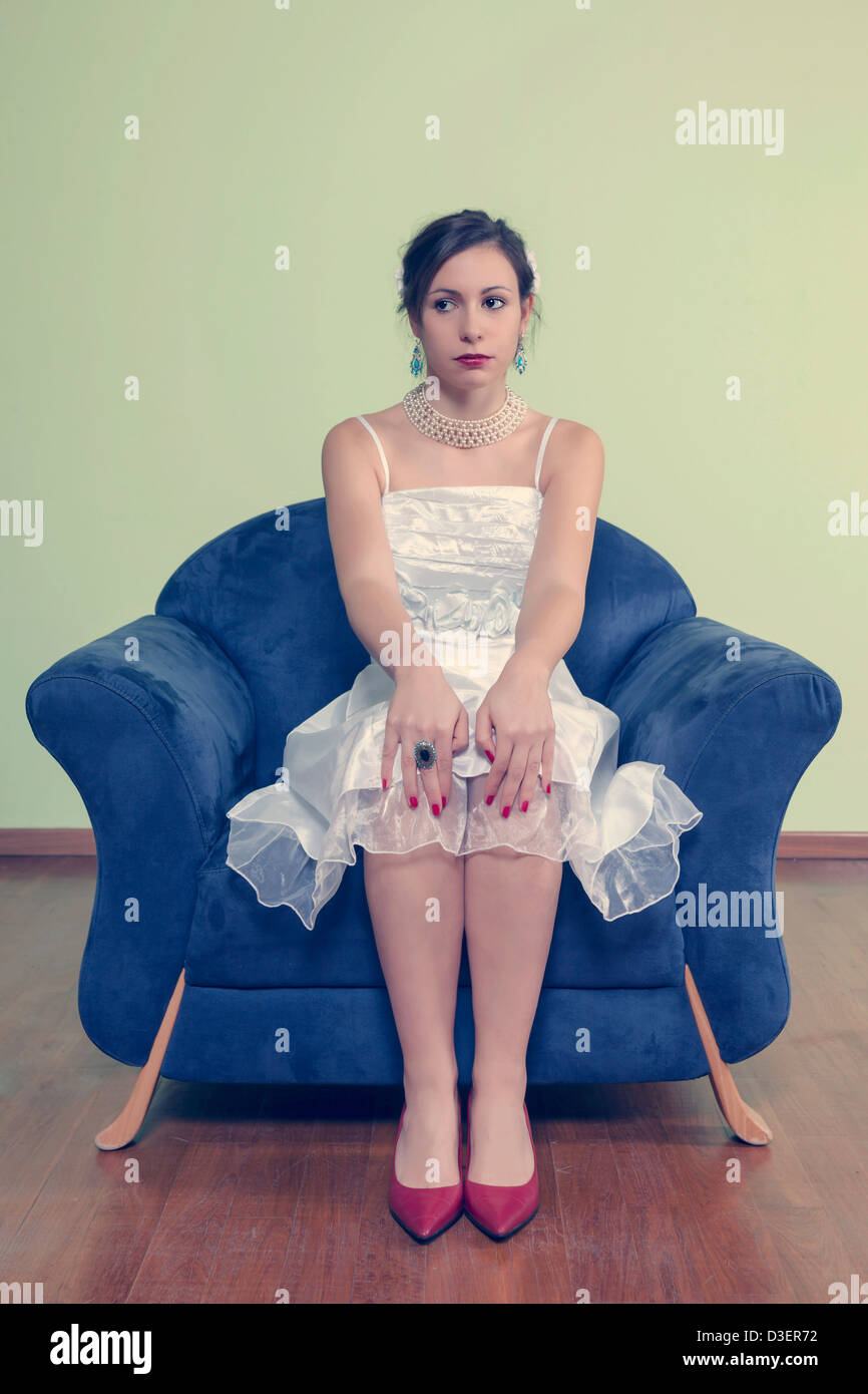 eine Frau in einem weißen Kleid sitzt auf einem blauen Sessel Stockfoto