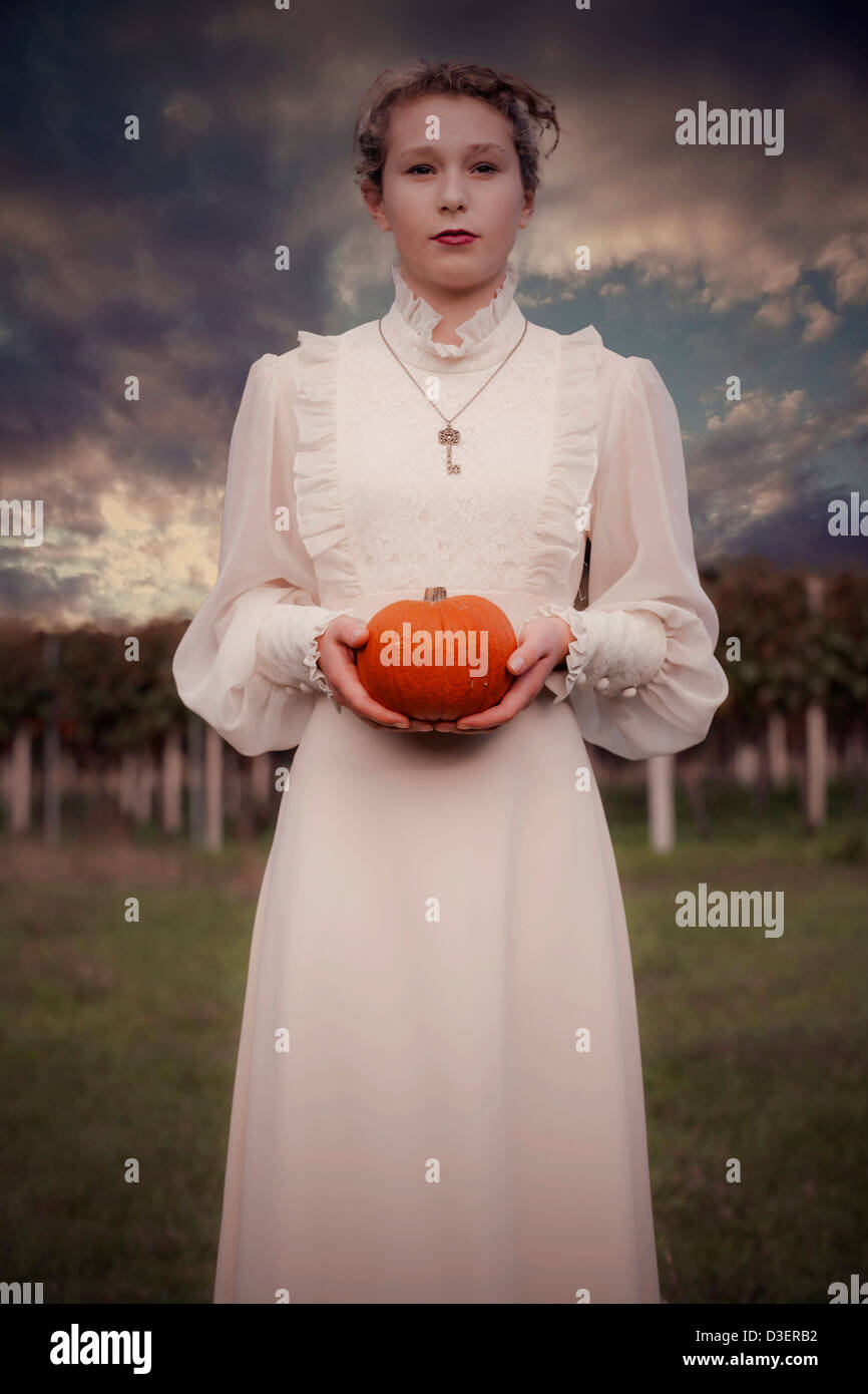eine Frau in einem viktorianischen Kleid hält einen Kürbis Stockfoto