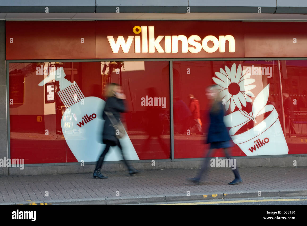 zwei Frauen gesehen in Bewegungsunschärfe zu Fuß in entgegengesetzte Richtungen außerhalb einer Banch von der High Street Einzelhändler, wilkinson Stockfoto