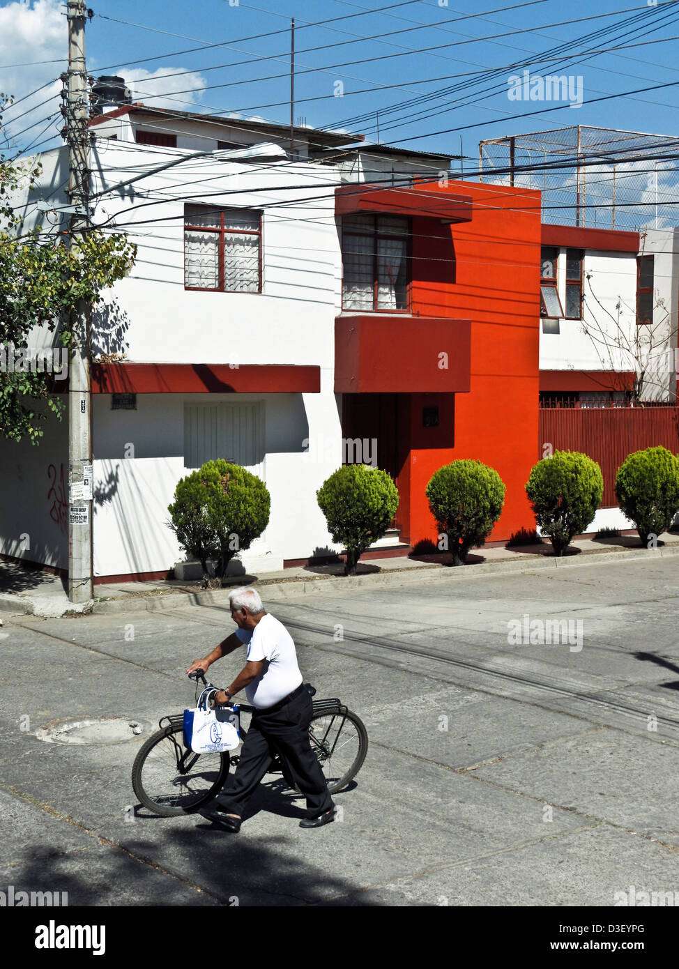 Mexikanische Mann mit silbernen Haaren Räder Fahrrad über Kreuzung vorbei modernes Haus mit markanten roten Akzent Wände Oaxaca Mexico Stockfoto