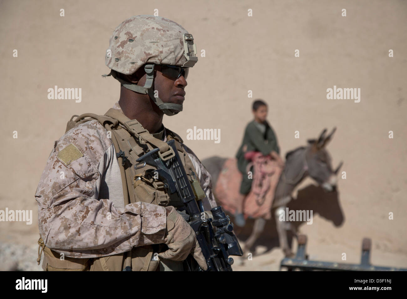 Ein US-Marine bietet Sicherheit bei einer afghanischen Nationalpolizei zivile Ordnung Checkpoint als ein Junge auf einem Esel wartet übergeben 8. Februar 2013 in der Kajaki district, Provinz Helmand, Afghanistan. Stockfoto