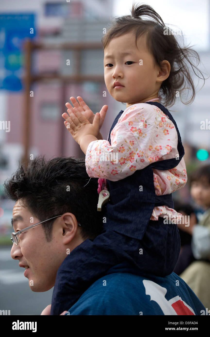 Junge Tochter bekommt einen guten Blick auf Vaters Schultern während einer Parade bei einem Festival in Japan. Stockfoto