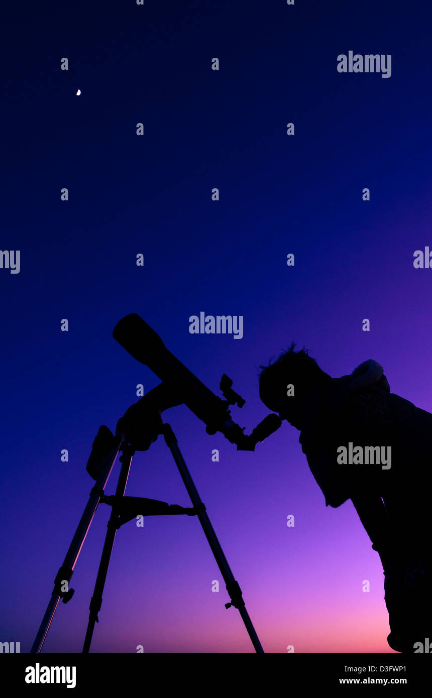 Die Silhouette eines Mädchens in der Dämmerung mit dem Mond-Overhead mit einem Teleskop beobachten. Stockfoto