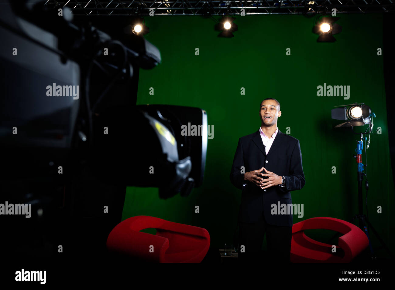 TV-Moderatorin in einem Greenscreen-Studio mit Fernsehkamera außerhalb des Fokus im Vordergrund. Stockfoto