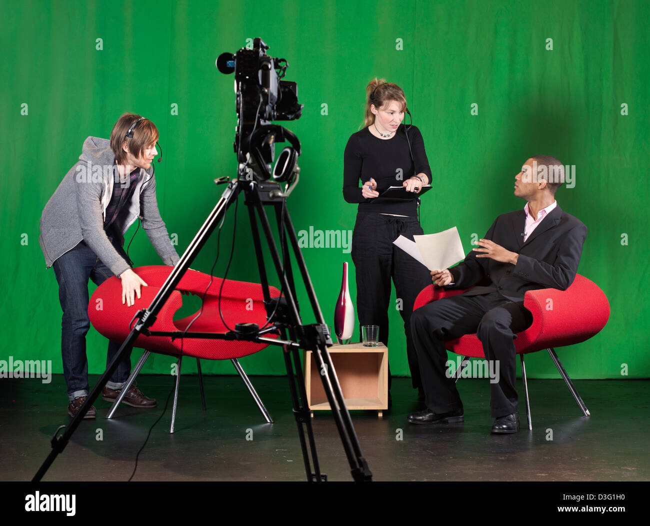 Ein Crew-Mitglied ordnet Möbel während der Aufnahmeleiter Gespräche an den Vortragenden über ein TV-Studio setzen. Stockfoto