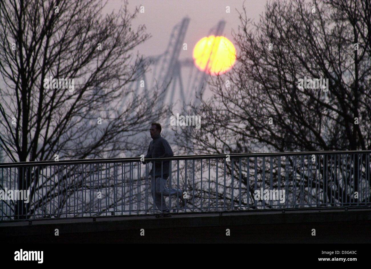(Dpa) - ein Jogger läuft über eine Fußgängerbrücke vor der kalten Morgensonne in Hamburg, 12. Februar 2003. Stockfoto