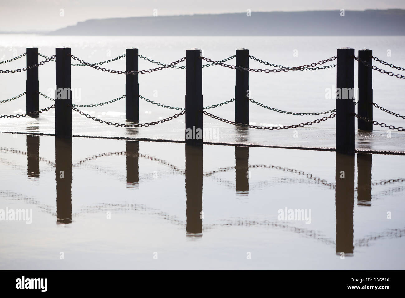 Zaun spiegelt sich in einer Lache des Wassers mit dem Meer im Hintergrund. Stockfoto